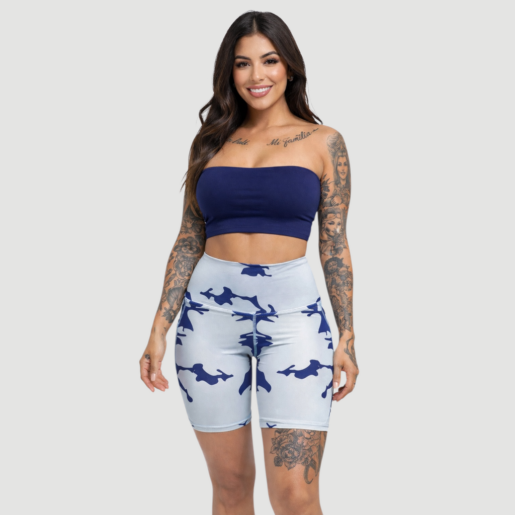 Woman wearing a blue bandeau top and white shorts with blue patterns on a plain background