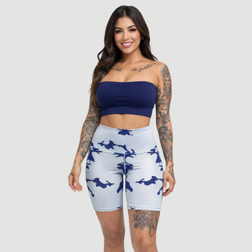 Woman wearing a blue bandeau top and white shorts with blue patterns on a plain background